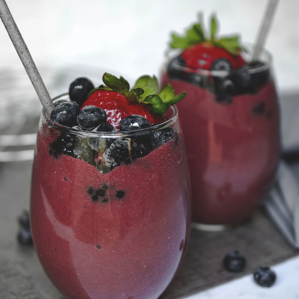 Two glasses of berry smoothie topped with fresh berries